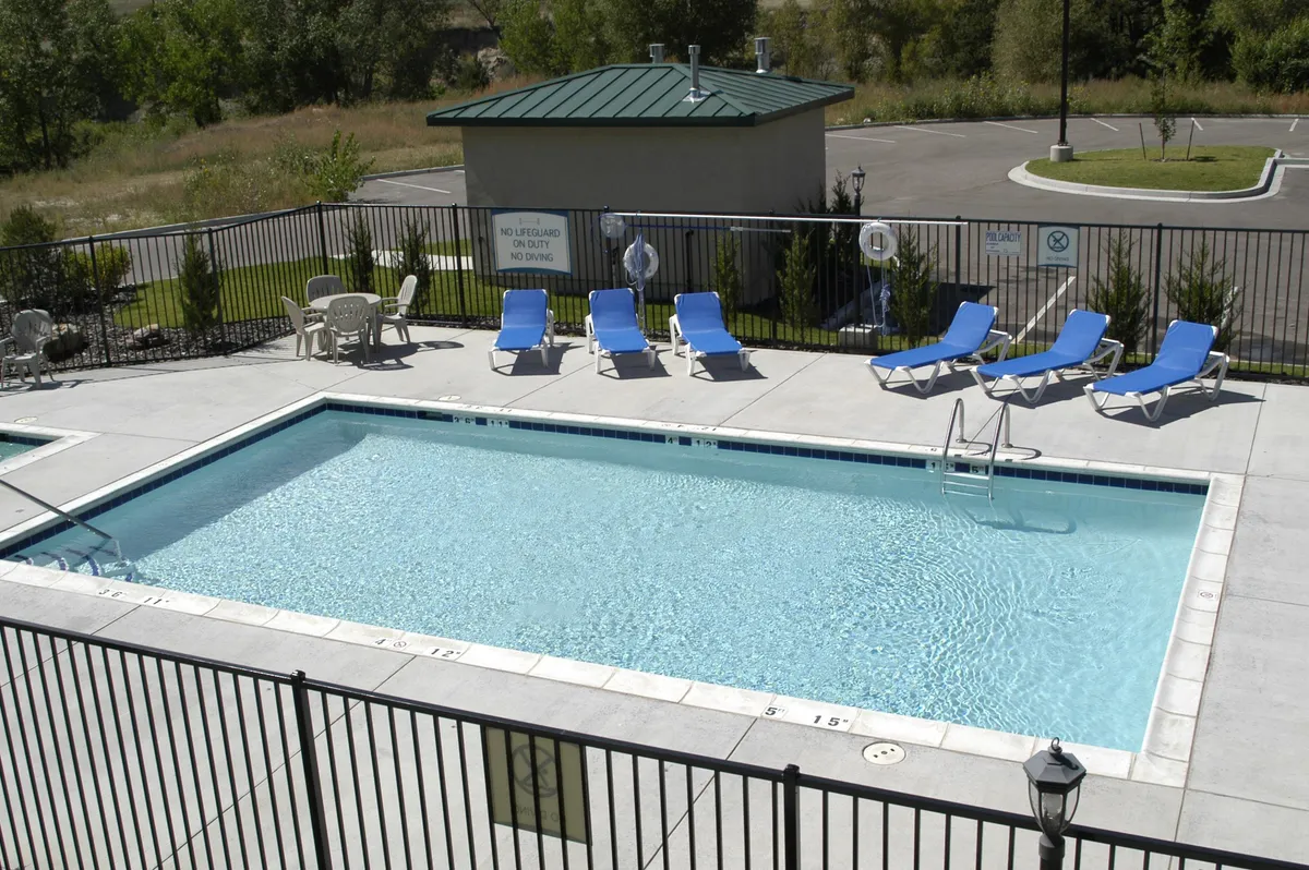 This image captures a vibrant outdoor swimming pool area surrounded by lounge chairs and a poolside fence. The scene includes guests enjoying leisurely activities such as swimming, sunbathing, and relaxing, suggesting an inviting social atmosphere suitable for gatherings and informal connections.