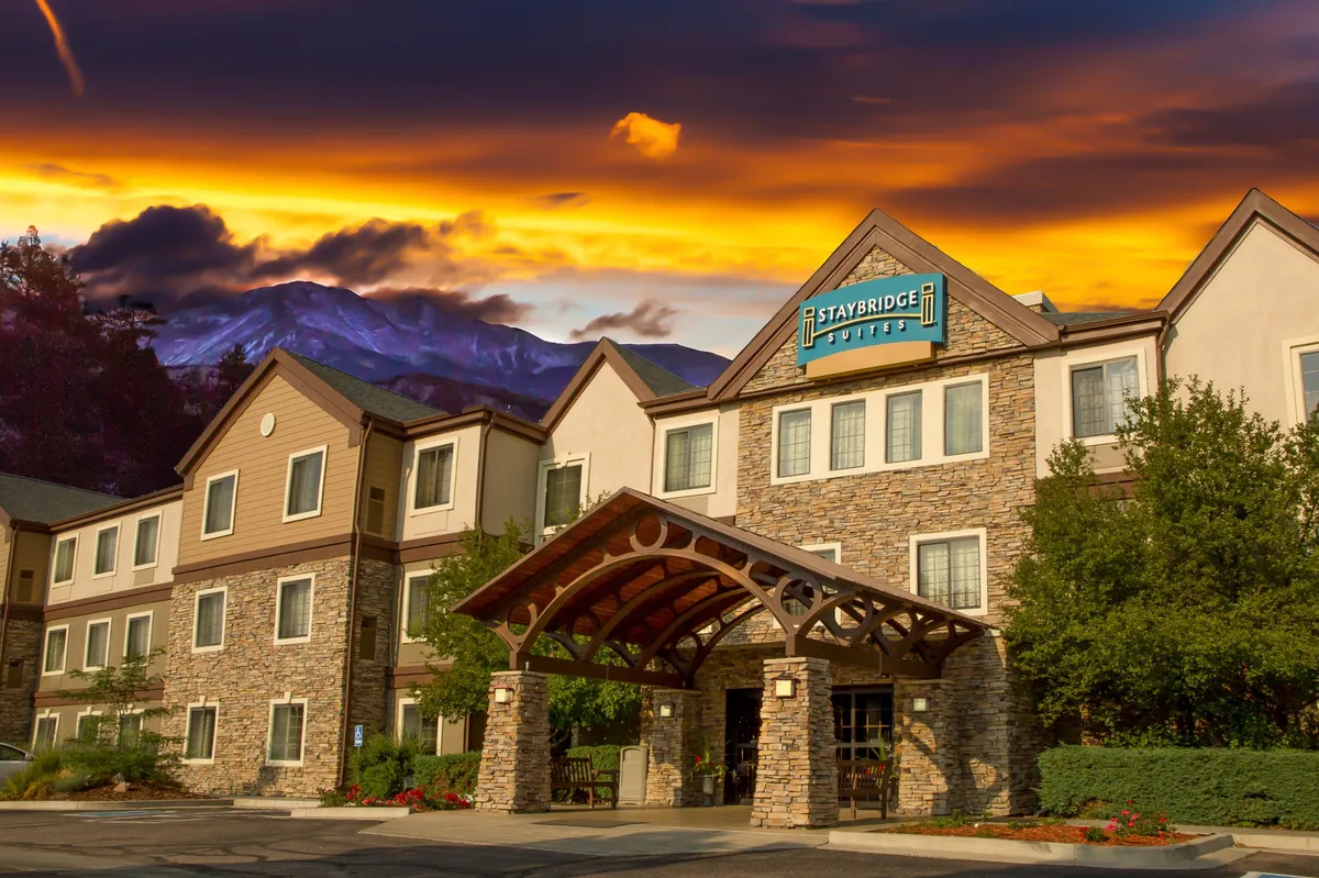 This exterior view features the condo-hotel's stone façade and wooden awning, complemented by branding signage. The setting is serene and welcoming, hinting at the broader inviting atmosphere that guests experience upon arrival, including evening receptions and outdoor social spaces.
