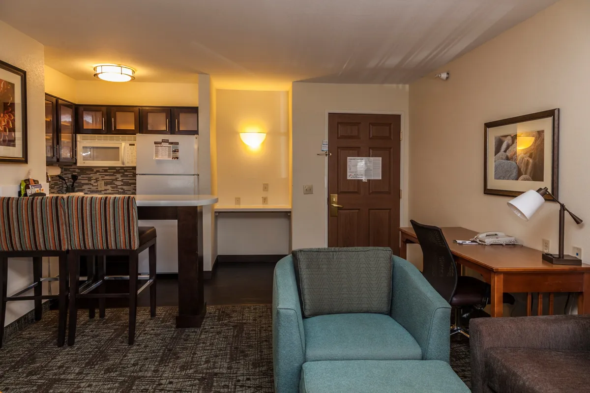 The image showcases a warm, inviting condo interior featuring a modern kitchenette with bar stools, a cozy seating area, and a dedicated desk space that together create a multifunctional living environment perfect for unwinding, entertaining, or working remotely.